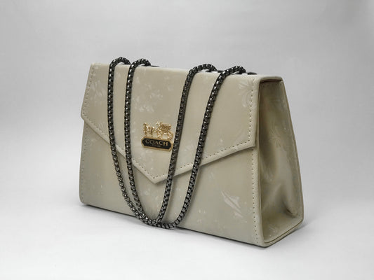Beige handbag with black chain strap on a white background