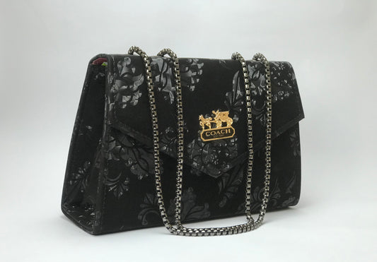 Black floral patterned handbag with gold chain strap on a white background